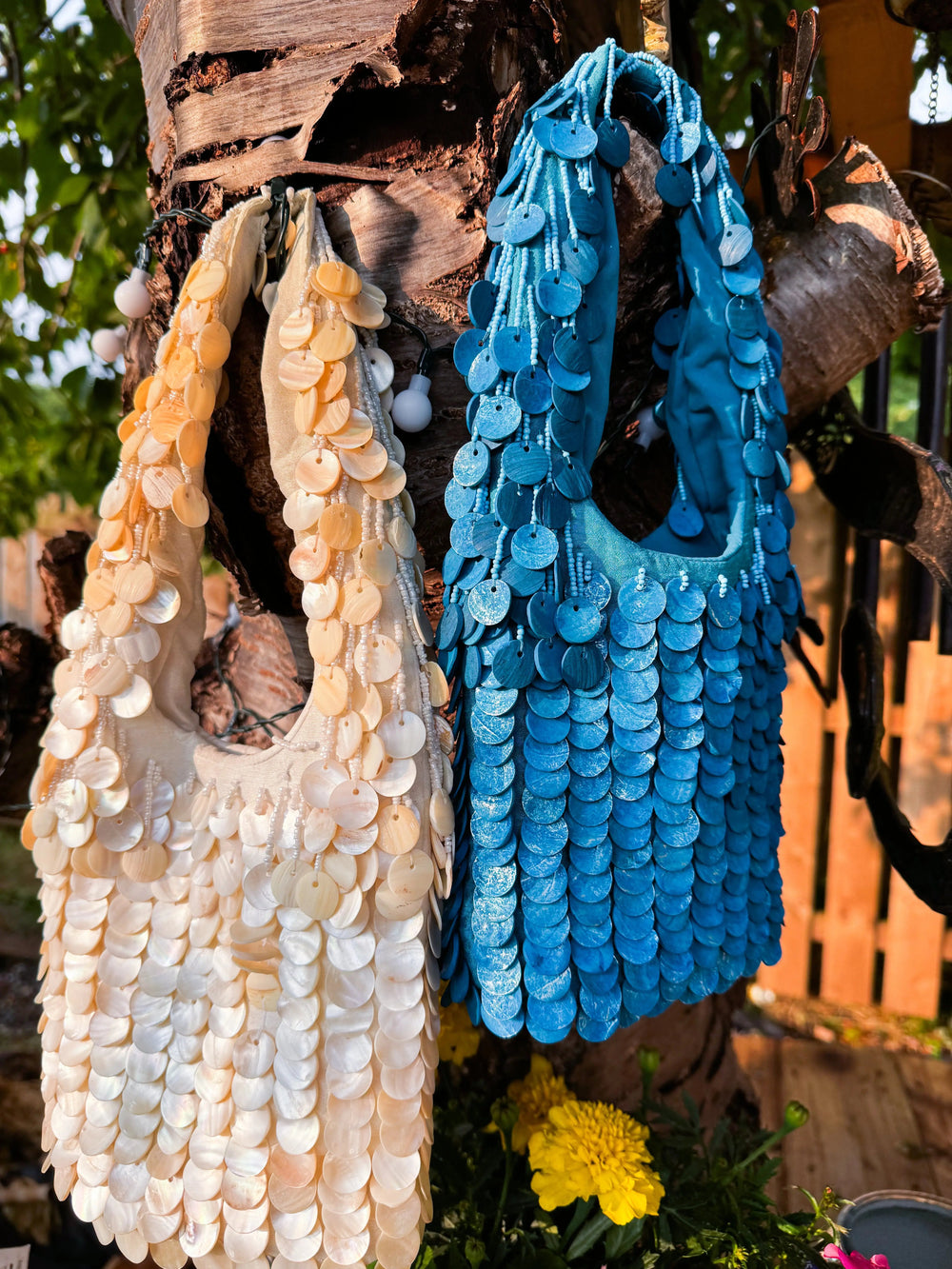 Oceana Shell Blue Bag and cream variant hanging on a tree, showcasing vibrant sequin detail. Ideal for alternative rave and festival fashion.
